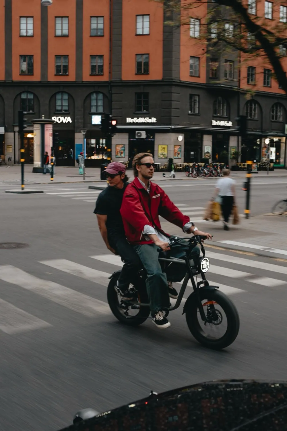 Two people riding a fat-tire e-bike across a crossing in Stockholm